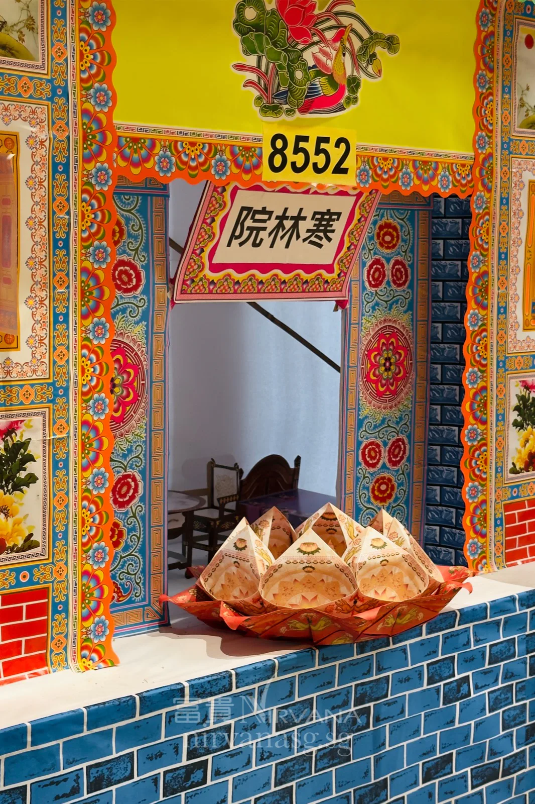 Ornate painted doorway of the Han Lin Yuan paper house with a plate of folded paper offerings on the sill