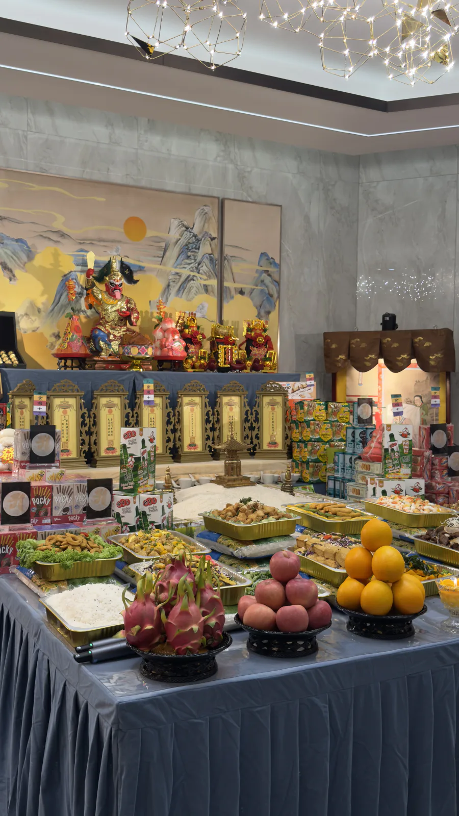 Close-up of the offering table at Nirvana's Seventh Month ceremony: fruit, snacks and rice laid before the figure of Mian Ran Da Shi and a row of memorial tablets